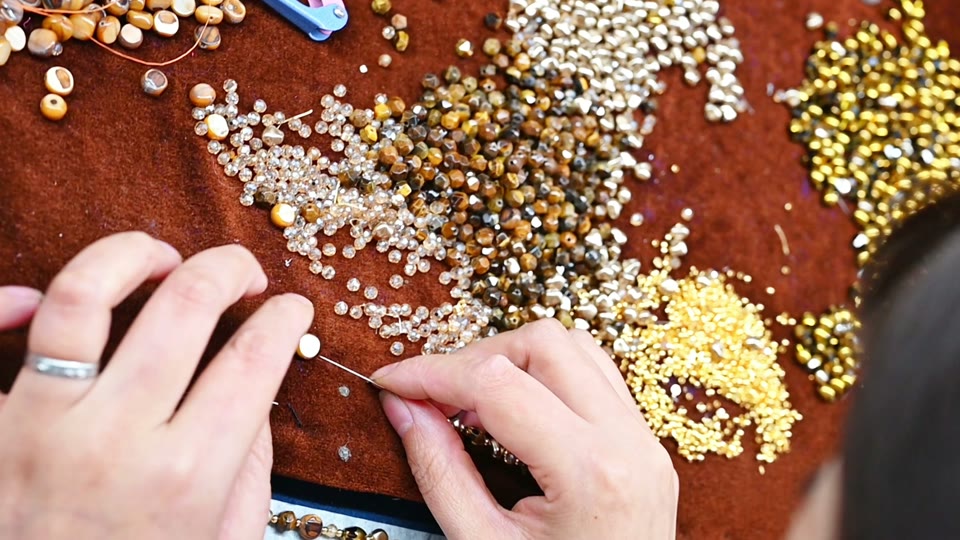Hands arranging jewelry components and beads.